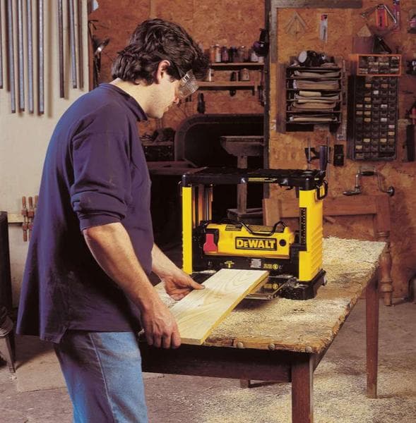 Person nutzt eine gelbe DEWALT DW733 Hobelmaschine an einer Werkbank in einer Werkstatt.