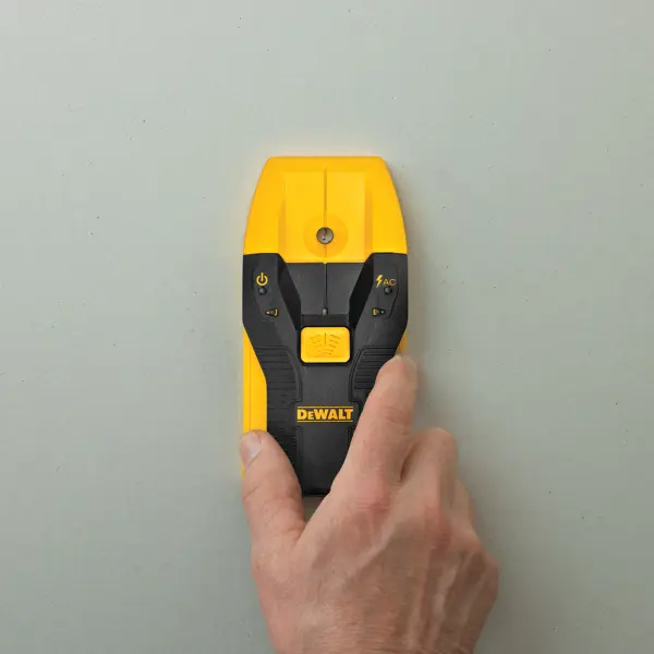 Eine Hand hält einen gelb-schwarzen DEWALT elektronischen Ortungsgerät an eine hellgraue Wand.