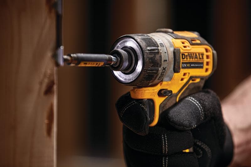 Ein DEWALT Akku-Bohrer schraubt eine Schraube ins Holz, gehalten von jemandem mit schwarzen Handschuhen.