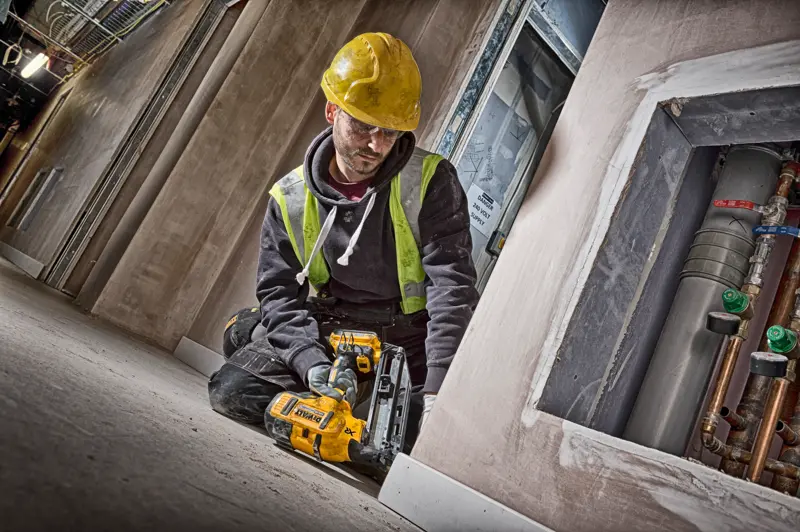 Bauarbeiter mit DEWALT DCN660N Nagler, gelber Helm und Sicherheitsweste auf Baustelle.