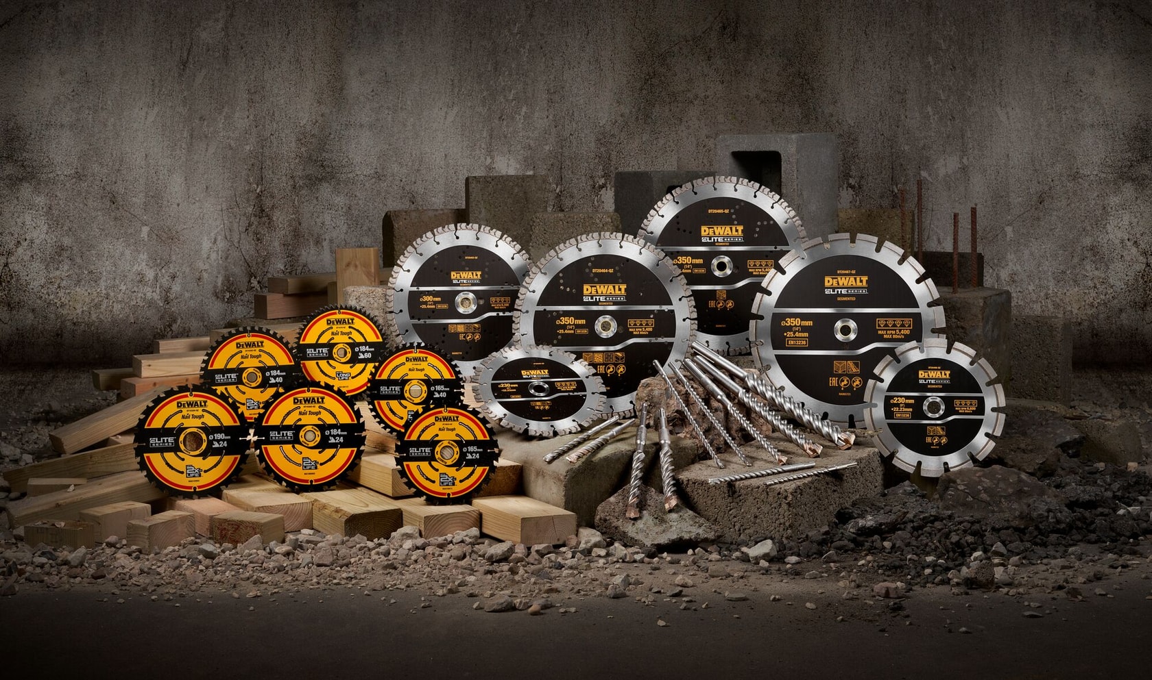 Verschiedene DEWALT-Kreissägeblätter und Bohrer werden auf Betonblöcken und Holzplanken vor einer rauen Industrie-Wand präsentiert.